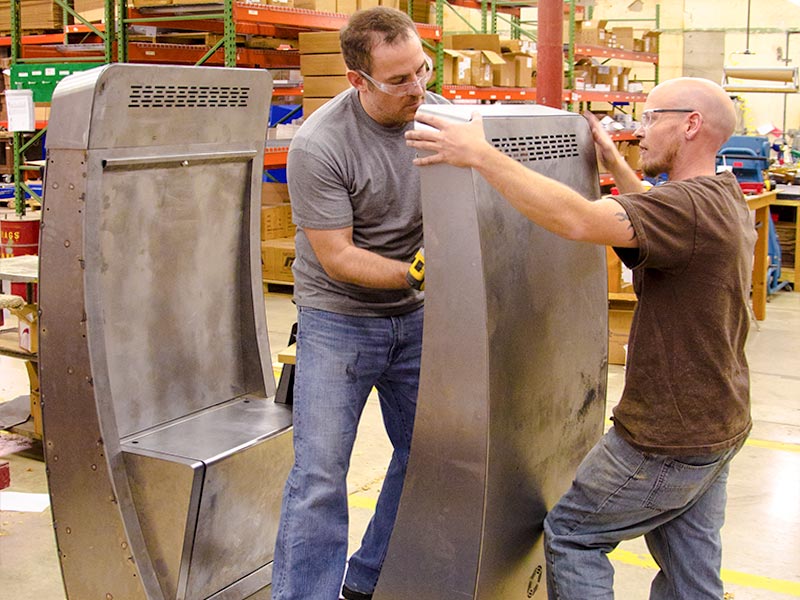 Two workers assemble a sleek health industry kiosk